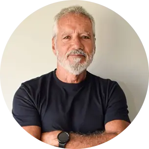 Fotografia de um homem branco de cabelos e barba grisalhos, utilizando uma camisa preta e com braços cruzados